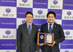 筑波大学でBest Faculty Memberの賞状を手に持った秋山先生と、人文社会系長が並んでいる写真