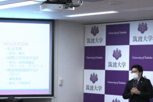 Best Faculty Member受賞者の秋山先生が写真右側に立ち、授賞式にてスライドを映写しながら講演をする様子